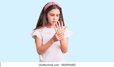 Cute hispanic child girl wearing casual white tshirt suffering pain on hands and fingers, arthritis inflammation 