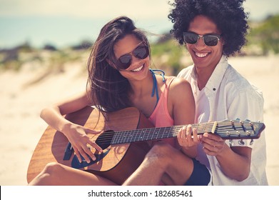 Cute hispanic couple playing guitar serenading on beach in love and embrace - Powered by Shutterstock