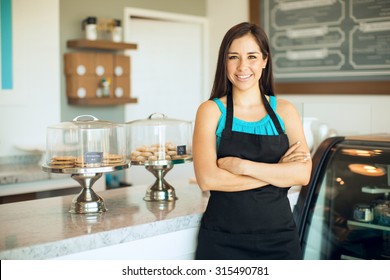 Cute Hispanic Female Business Owner Standing In Front Of Her Cake Shop And Smiling