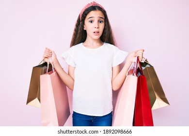 Cute Hispanic Girl Holding Shopping Bags Clueless And Confused Expression. Doubt Concept. 