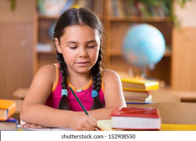 Cute Hispanic Girl Writing In Notebook In Classroom At School