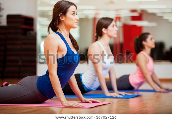 Cute Hispanic women practicing the cobra pose\
during their yoga class in a\
gym