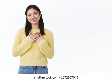 Cute humble and grateful asian girl thanking for congratulations, press hands to heart and smiling blushing from happiness and joy receiving gifts, looking touched, standing against white background