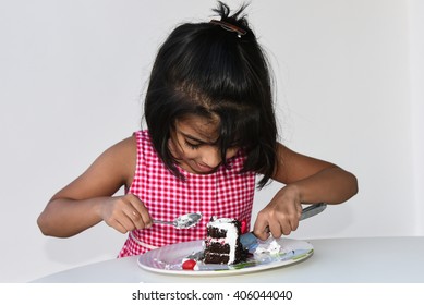 Cute Hungry Happy Smiling Little Girl/ Kid/ Child Eating/ Cutting Tasty Black Forest Cake/ Pastry Cherry, India, Asia. Playful Young/ Small Indian Girl Sitting Table Holding Table Knife, Birthday Cake