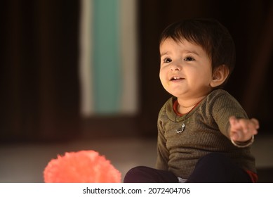 Cute Indian baby girl in a playful mood, showing teeth while sitting and smiling