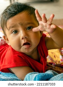 Cute Indian Baby Lying On Bed Sheet Over A Mat Extending Arm Towards The Camera  Selective Focus On Baby's Face 