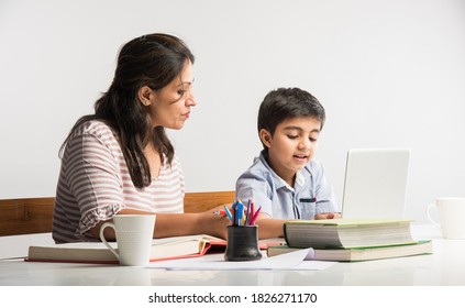 Cute Indian boy with mother doing homework at home using laptop and books - online schooling concept