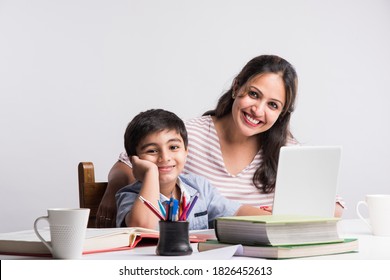 Cute Indian boy with mother doing homework at home using laptop and books - online schooling concept