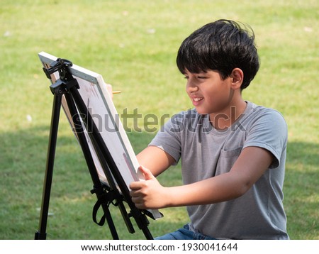 Cute Indian child painting with watercolors outdoor in the nature park. Concept of education outside of school