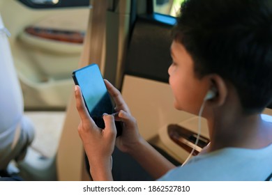 Cute indian child sitting in car and using smart phone and headphones gadget