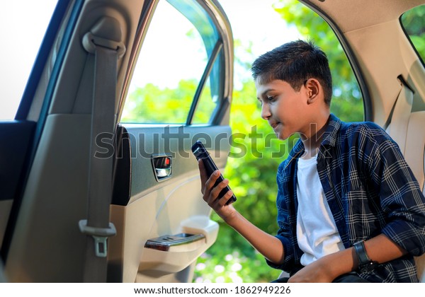 Cute indian child sitting in car and using smart
phone and headphones
gadget