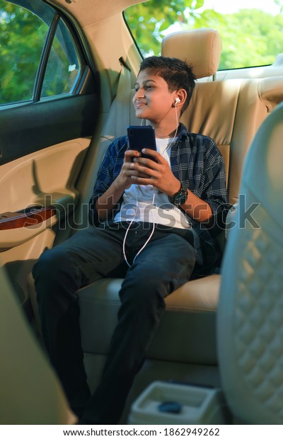Cute indian child sitting in car and using smart\
phone and headphones\
gadget