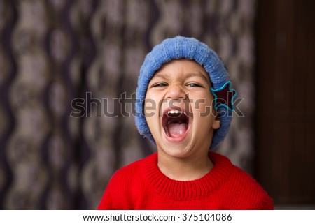 Cute Indian Kid striking a pose wearing red sweater and blue cap with a big laugh available with clipping path