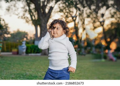 Cute Indian Little Child Face Closeup On Green Grass In Summertime. Funny Little Kid Portrait With Mobile Phone, Smartphone On Nature. Happy Childhood.