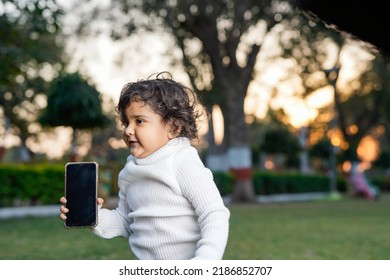 Cute Indian Little Child Face Closeup On Green Grass In Summertime. Funny Little Kid Portrait With Mobile Phone, Smartphone On Nature. Happy Childhood.