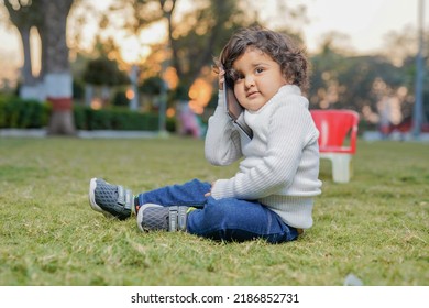 Cute Indian Little Child Face Closeup On Green Grass In Summertime. Funny Little Kid Portrait With Mobile Phone, Smartphone On Nature. Happy Childhood.