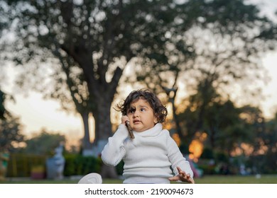 Cute Indian Little Child Face Closeup On Green Grass In Summertime. Funny Little Kid Portrait With Mobile Phone, Smartphone On Nature. Happy Childhood.