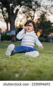 Cute Indian Little Child Face Closeup On Green Grass In Summertime. Funny Little Kid Portrait With Mobile Phone, Smartphone On Nature. Happy Childhood.