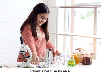 Cute Indian school girl in India traditional dress costume doing science experiments in laboratory, young scientist kid with microscope and lab equipment learning biologics and chemistry in classroom. - Powered by Shutterstock