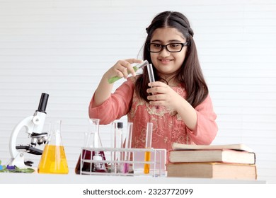 Cute Indian school girl in India traditional dress costume doing science experiments in laboratory, young scientist kid with microscope and lab equipment learning biologics and chemistry in classroom. - Powered by Shutterstock