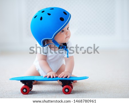 cute infant baby girl in protective helmet outfit ready to ride skateboard, extreme sport concept