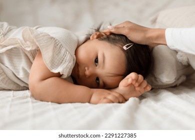 Cute Japanese Baby Daughter Lying While Mom's Hand Stroking Her Head In Modern Bedroom At Home. Mother Calming Down And Caring For Toddler Infant. Motherhood And Babysitting - Powered by Shutterstock