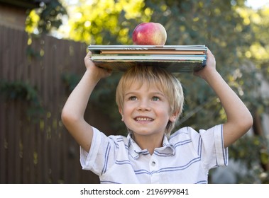 Cute Joyful 6 Year Old Boy Is Holding A Stack Of Books And A Big Apple On His Head. Reading Books, Interesting Childhood, Inquisitive Child, Knowledge Is Power. Hello School. Book Day