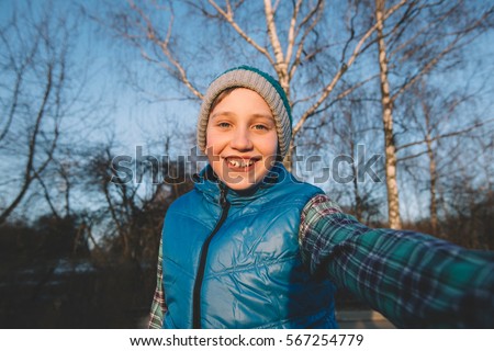 Cute kid boy having fun after school and making selfie. Teenager walking in a park and taking self-portrait with a smartphone.