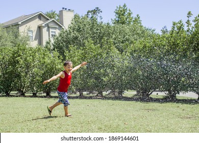 Cute Kid Boy  Splashing With Gardening Hose On Backyard On Summer Day. Child Playing With Water Outside At Home Yard. Candid Authentic Real Life Moment Of Funny Family Activity.