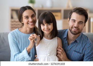Cute kid daughter holding keys from new house looking at camera with mom and dad, child girl and parents home owners enjoying buying flat, happy family mortgage, real estate ownership, portrait
