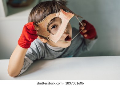 Cute Kid In Disguise With DIY  Cardboard Superhero Mask At Home. Boy With Creative Halloween Costume Or Festive Apparel For Children Theater. Playful Spirit Concept. Home Celebration With Family.