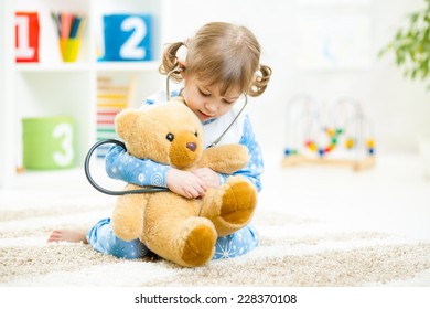 Cute kid girl playing doctor with plush toy at home
