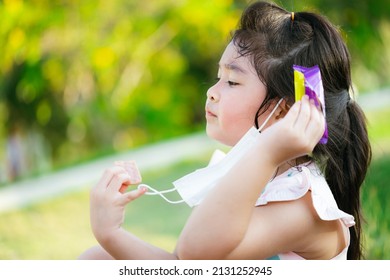 Cute kid girl is taking off her face mask as she eats snacks in public park. Child are hungry. Children 5 years old. Empty space for text.