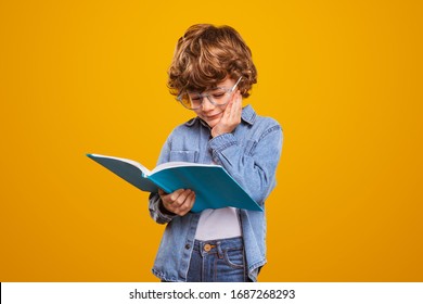 Cute Kid With Hand Near Cheek Reading Fascinating Book During School Studies Against Yellow Background