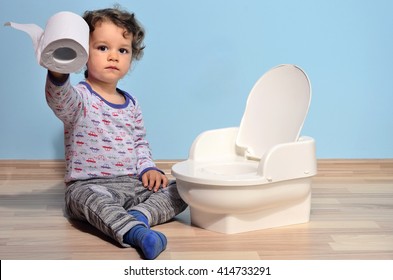 Cute kid potty training for pee and poo.Baby toddler sitting on the floor near a potty and playing with toilet paper