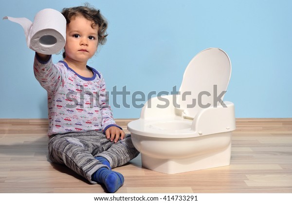 Cute kid\
potty training for pee and poo.Baby toddler sitting on the floor\
near a potty and playing with toilet\
paper