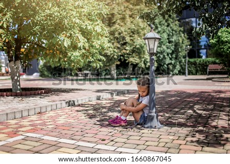 Cute kid sitting under streetlights on the ground with different colored patterned paving slabs, representative patio tiles alley, street exterior design. Sidewalk pavement pattern.