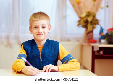 Cute Kid With Special Need Sitting At The Desk In Classroom