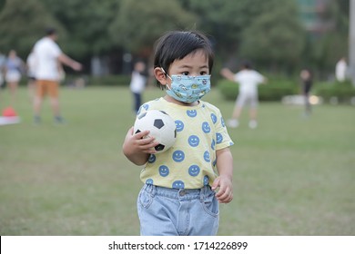 A Cute Kid Is Wearing Mask To Prevent Corona Virus At The Park. He Is Holding Soccer Ball And Looking Forward. He Looks Serious.