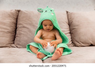 A Cute Kid Wrapped In A Towel Sits On The Bed. Baby In A Bath Towel.