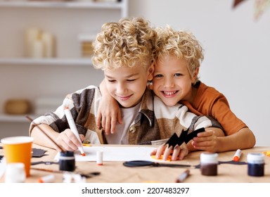 Cute kids  boys  making Halloween home decorations   while sitting at wooden table, children painting pumpkins and making paper cuttings