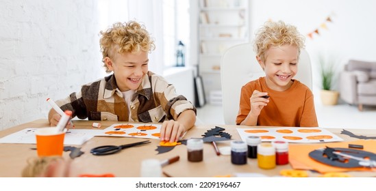 Cute Kids  Boys  Making Halloween Home Decorations   While Sitting At Wooden Table, Children Painting Pumpkins And Making Paper Cuttings