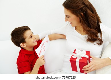 Cute lad with congratulating card looking at his mother with giftbox - Powered by Shutterstock