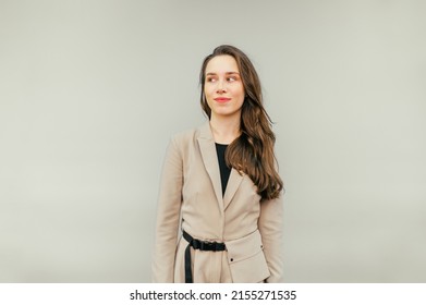 Cute Lady In A Beige Suit Stands On A Beige Background And Looks Away With A Sarcastic Smile On Her Face. Copy Space