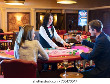 Cute Lady Casino Dealer At Poker Table. Happy Couple Is Playing Black Jack.