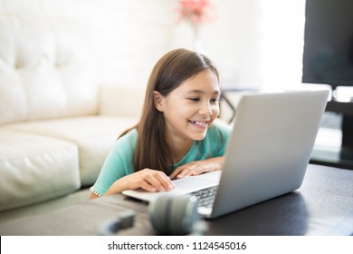 Cute Latin Girl Smiling And Sitting At Home Using A Laptop Computer To Do Her Class Work And Browse The Internet