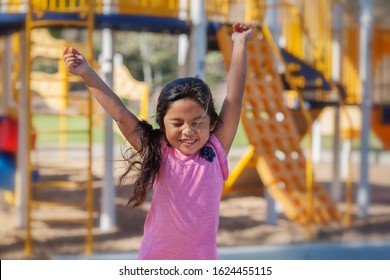 A Cute Latino Girl Jumping With Joy As She Plays In A Kids Playground.