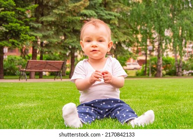 Cute laughing blonde baby girl 1 year old top having fun sitting in green grass outdoors. 