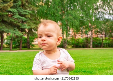 Cute laughing blonde baby girl 1 year old top having fun sitting in green grass outdoors. 