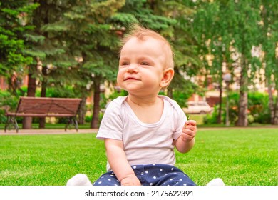 Cute laughing blonde baby girl 1 year old top having fun sitting in green grass outdoors.  Happy little child laughs nicker in meadow.